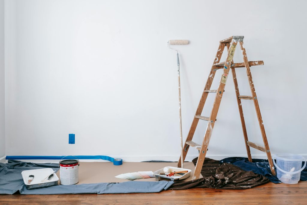 pexels-photo-7218525-7218525 A room prepared for renovation with a ladder, paint supplies, and drop cloth.